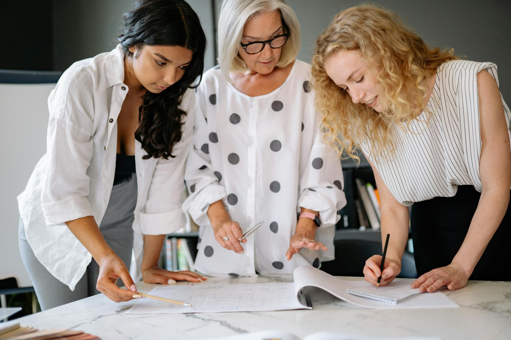 Three women working together over documents on a marble table indoors, showcasing teamwork and planning.